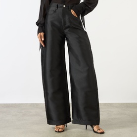 Model wearing Marques Almeida Mikado Boyfriend Trousers in black satin with wide-cut legs, paired with black heeled sandals and sheer top.