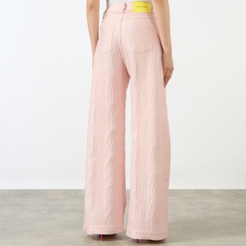 Model wearing Marques Almeida Textured Brocade Boyfriend Jeans in pink, wide-leg cut with cable-effect texture, yellow logo badge visible at