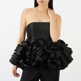 Model wearing Marques Almeida Ruffle Bustier Top in black; strapless fitted satin bodice with voluminous ruffled ribbon peplum hem