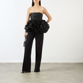 Model wearing Marques Almeida Ruffle Bustier Top in black strapless satin with ruffled peplum hem, styled with wide-leg trousers and clutch bag