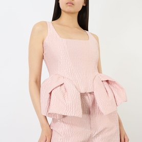 Model wearing Marques Almeida Textured Brocade Peplum Corset Top in pink, square neckline, sleeveless, styled with matching wide-leg trousers