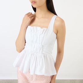 Model wearing Marques Almeida Wrinkled Gathered Top in white with square neckline, shirred bodice and peplum hem, styled with pink trousers.