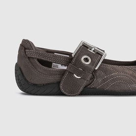 Puma matte bronze black women's flat shoe close-up, textured upper with silver buckle strap detail and black rubber sole.