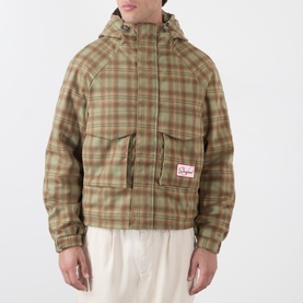 Model wearing Storefront Script Logo Flannel Utility Jacket in green check with hood, flap pockets and logo patch, styled with cream trousers.