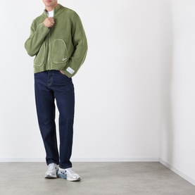 Model wearing Storefront Fisherman Script Logo Zip Sweater in olive, styled with dark indigo jeans and white trainers