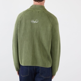 Model wearing Storefront Fisherman Script Logo Zip Sweater in olive, showing ribbed back with embroidered script logo, styled with dark jeans.