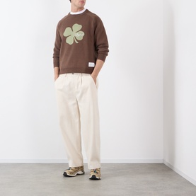 Model wearing Storefront brown cotton knit sweatshirt with green clover graphic, styled with cream wide-leg trousers and chunky trainers.