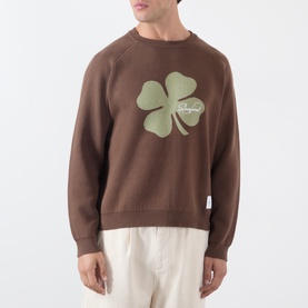 Model wearing Storefront brown cotton sweatshirt with oversized green four-leaf clover graphic, styled with cream trousers.