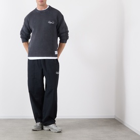 Model wearing Storefront Fisherman Script Logo Sweater in Charcoal with matching black joggers and grey trainers.
