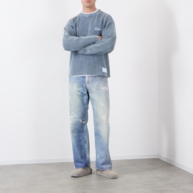 Model wearing Storefront Fisherman Script Logo Sweater in blue with distressed light-wash jeans and grey suede mules.