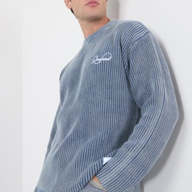 Model wearing Storefront Fisherman Script Logo Sweater in blue, featuring ribbed knit texture, crew neckline, and embroidered script logo on chest.