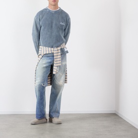 Model wearing Storefront Fisherman Script Logo Sweater in blue with washed finish, styled with light-wash jeans and a striped shirt tied at the waist.