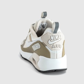 Nike Air trainer in light bone and off-white, rear three-quarter view showing textured heel panel, grey accents and white rubber sole.