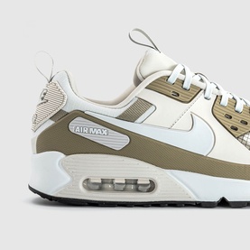 Nike Air Max 90 trainer in light bone and neutral tan, white leather upper, Air Max cushioned sole, black outsole, close-up detail shot
