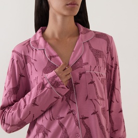 Model wearing Chelsea Peers Modal Giraffe Long Pyjama Set in Giraffe Pink, showing revere collar, button front and piped trim detail.