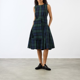 Model wearing JW Anderson dress in navy and green tartan check, sleeveless with tie waist and full pleated skirt, styled with black loafers.