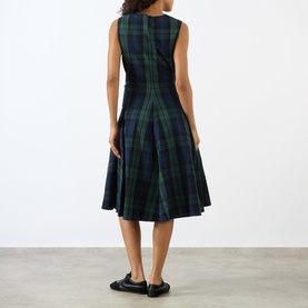 Model wearing JW Anderson dress in navy and green tartan plaid, sleeveless A-line silhouette, rear view, styled with black loafers.