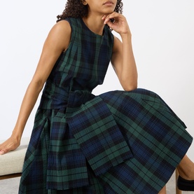 Model wearing JW Anderson dress in navy and green tartan check, sleeveless with tie waist detail, midi length in 100% cotton.