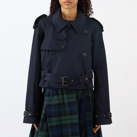 Model wearing JW Anderson navy cotton cropped trench jacket with double-breasted buttons and belted waist, styled with green tartan skirt.