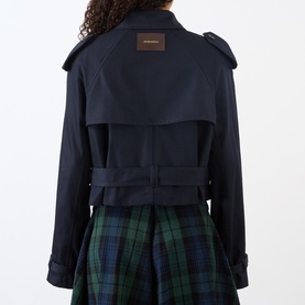 Model wearing JW Anderson navy cotton jacket, back view, showing belted waist, epaulettes and brown logo patch, styled with green tartan skirt.