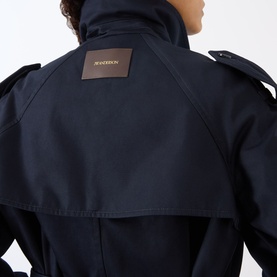Model wearing JW Anderson navy cotton jacket, back view showing branded leather patch, epaulette shoulders and high collar detail.