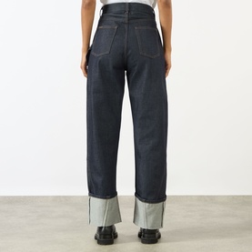 Model wearing JW Anderson Twisted Wide Leg Trousers in indigo, featuring wide leg fit, turned-up hem with contrast lining, and back pockets.