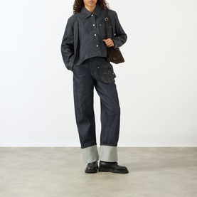 Model wearing JW Anderson Flare Hem Denim Shirt in indigo with wide-leg jeans, styled with a brown bag and black loafers