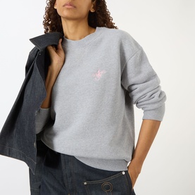 Model wearing JW Anderson Anchor Logo Sweatshirt in mid grey melange, crew neck with pink anchor embroidery, styled with dark denim jacket and jeans.