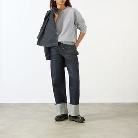 Model wearing JW Anderson Anchor Logo Sweatshirt in Mid Grey Melange, styled with dark indigo jeans, grey boots and a grey jacket.