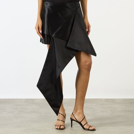 Model wearing JW Anderson Cross Drape Asymmetrical Mini Skirt in black with draped front and asymmetric hem, styled with strappy heeled sandals.