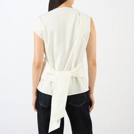 Model wearing JW Anderson ivory cotton sleeveless top, shown from behind with statement self-tie belt detail at waist, styled with dark jeans.
