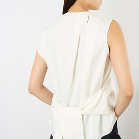 Model wearing JW Anderson ivory cotton sleeveless top, back view showing draped tie-waist detail and centre pleat