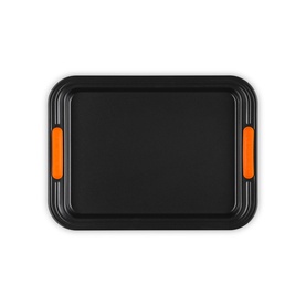 Le Creuset Small Baking Tray 27cm in Satin Black, rectangular non-stick carbon steel with orange silicone handles, overhead view