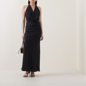Model wearing Rotate black halterneck maxi dress with all-over dot print, styled with strappy heels and a small shoulder bag.
