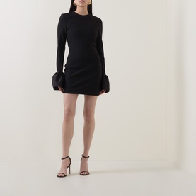 Model wearing Rotate black long-sleeve mini dress with feather cuff detail, styled with black strappy heels and clutch bag
