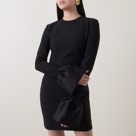 Model wearing Rotate black mini dress with long flared sleeves and oversized satin bow detail at hip, gold earrings visible