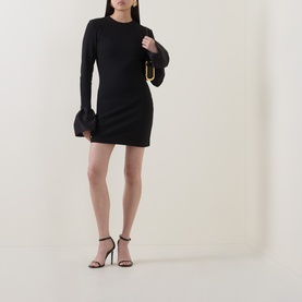 Model wearing Rotate black mini dress with sheer flared cuffs, styled with black strappy heels and small gold-hardware shoulder bag.