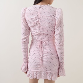 Model wearing Rotate barely pink ruched mini dress with long sleeves, polka dot print, tie-back detail and frill hem, back view.