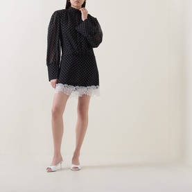 Model wearing Rotate black polka dot mini dress with lace hem trim and high neck, styled with white heeled mules