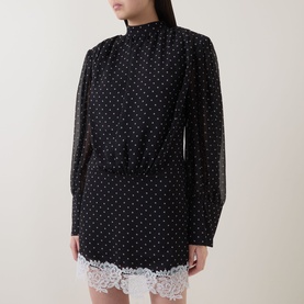 Model wearing Rotate black polka dot mini dress with high neck, long sleeves, elasticated waist and white lace hem trim