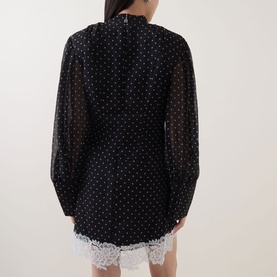 Model wearing Rotate black polka dot sheer dress with puff sleeves, shown from behind, styled with white lace hem detail