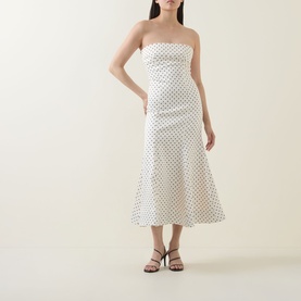 Model wearing Rotate Dress in Egret dot print, strapless midi length with flared hem, styled with black strappy heeled sandals