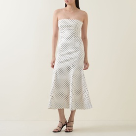 Model wearing Rotate Dress in Egret white polka dot print, strapless midi length with flared hem, styled with black strappy heels
