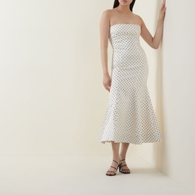 Model wearing Rotate Dress in Egret dot print, strapless midi silhouette with flared hem, styled with black strappy flat sandals
