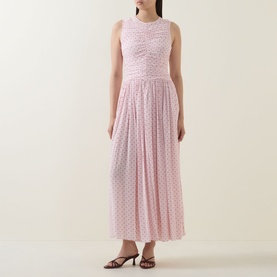 Model wearing Rotate barely pink sleeveless maxi dress with ruched bodice, pleated skirt and polka dot texture, styled with black heeled sandals.