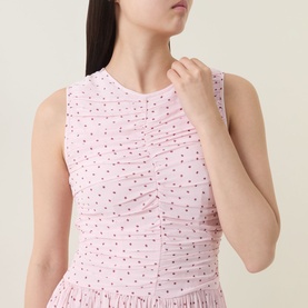 Model wearing Rotate barely pink sleeveless ruched dress with red polka dot print, featuring pleated hem detail