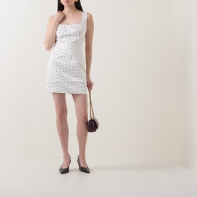 Model wearing Rotate Dress in Egret white polka dot print mini style, styled with dark mini bag and black kitten heels.