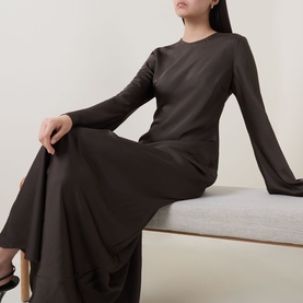 Model wearing Rotate dress in Black Olive, long-sleeve style with flared cuffs and flared midi skirt, seated pose