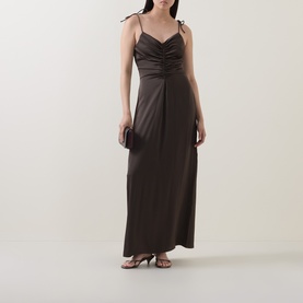 Model wearing Rotate Black Olive maxi dress with ruched bodice, tie shoulders, and side drape, styled with strappy heels and clutch bag.