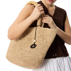Model carrying Whistles beige woven raffia tote bag with rope handles and black resin ring charm detail, styled with brown vest top.